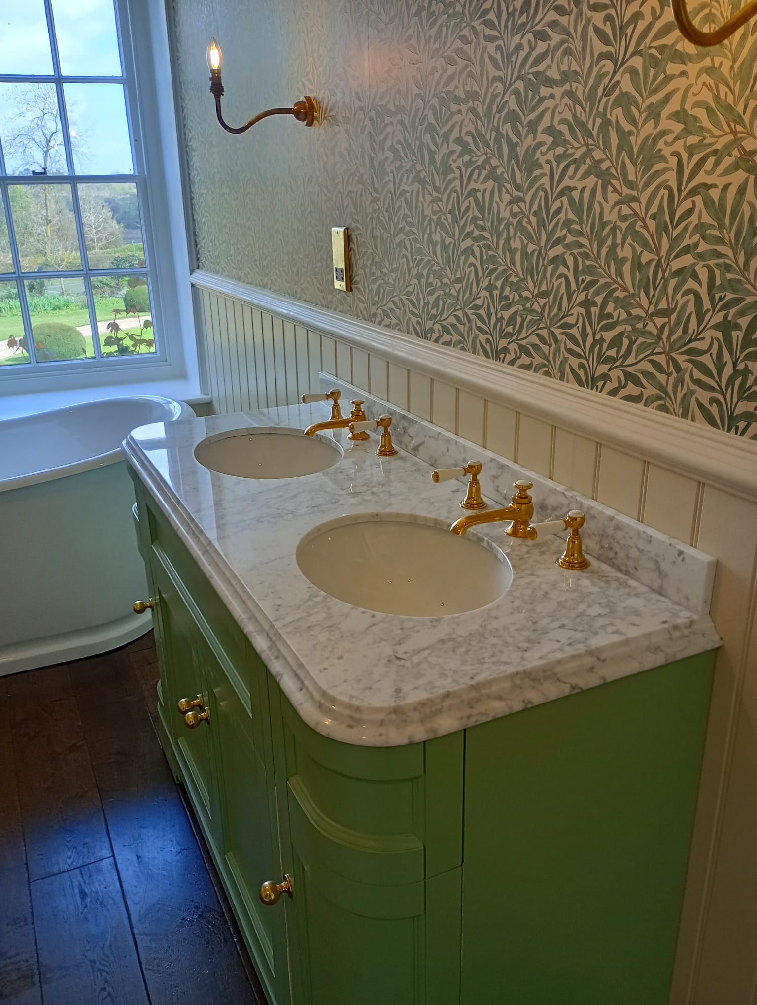 Double vanity with green cabinetry and a garden view