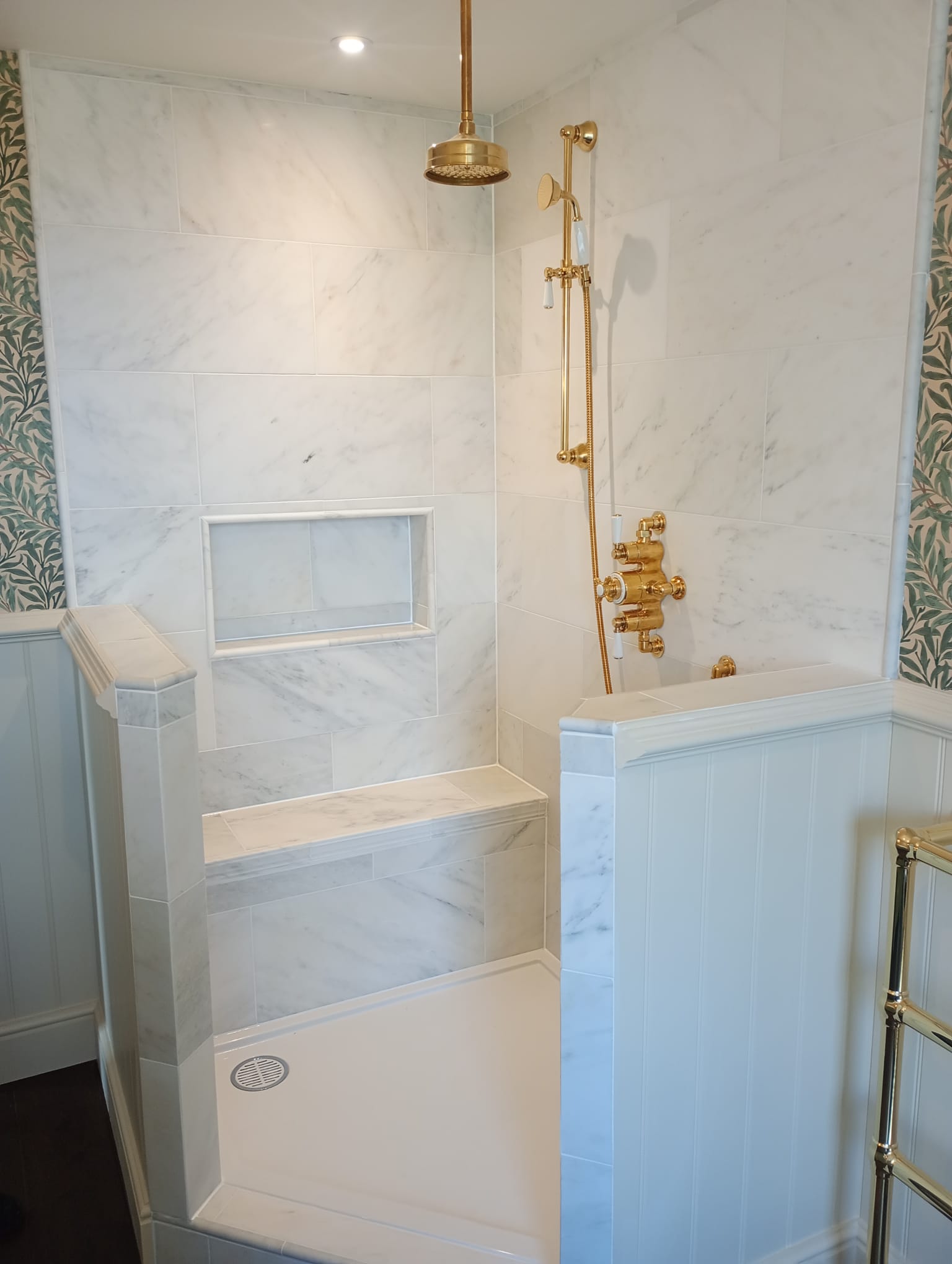 Luxury tiled shower enclosure with brass fittings and floral wallpaper