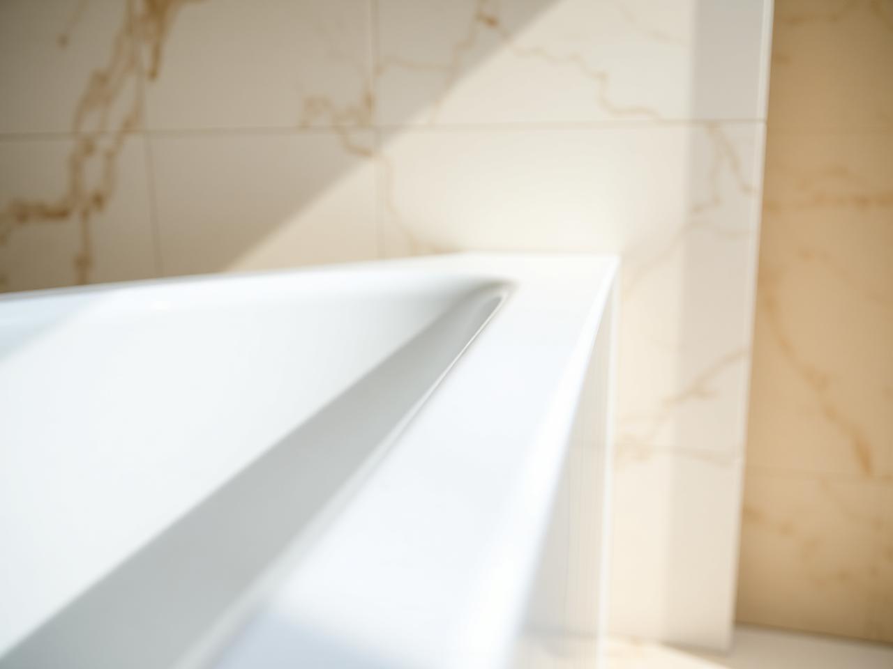 Precision mastic and silicone sealant work along a marble bath